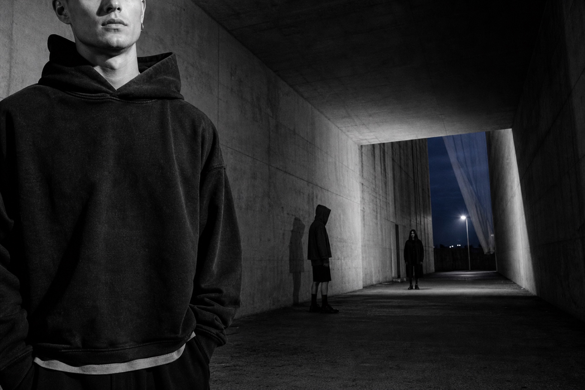 Models in black oversized clothing inside a monumental concrete passage